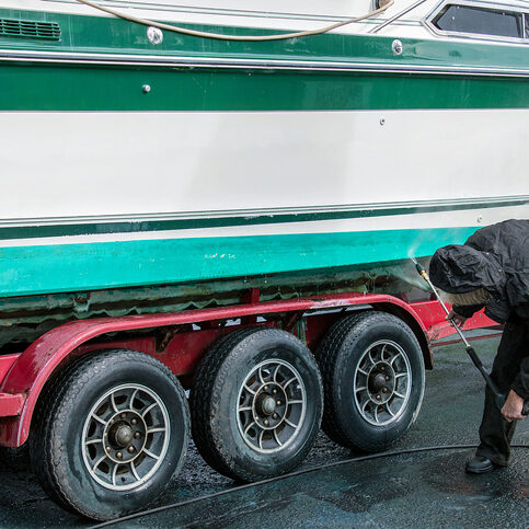 man wearing black waterproof suit while cleaning hull of power boat